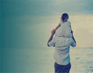 Young girl on fathers shoulders facing the sea