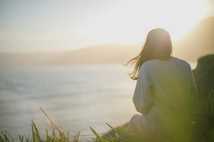 woman sitting on clifftop facing sun in distance
